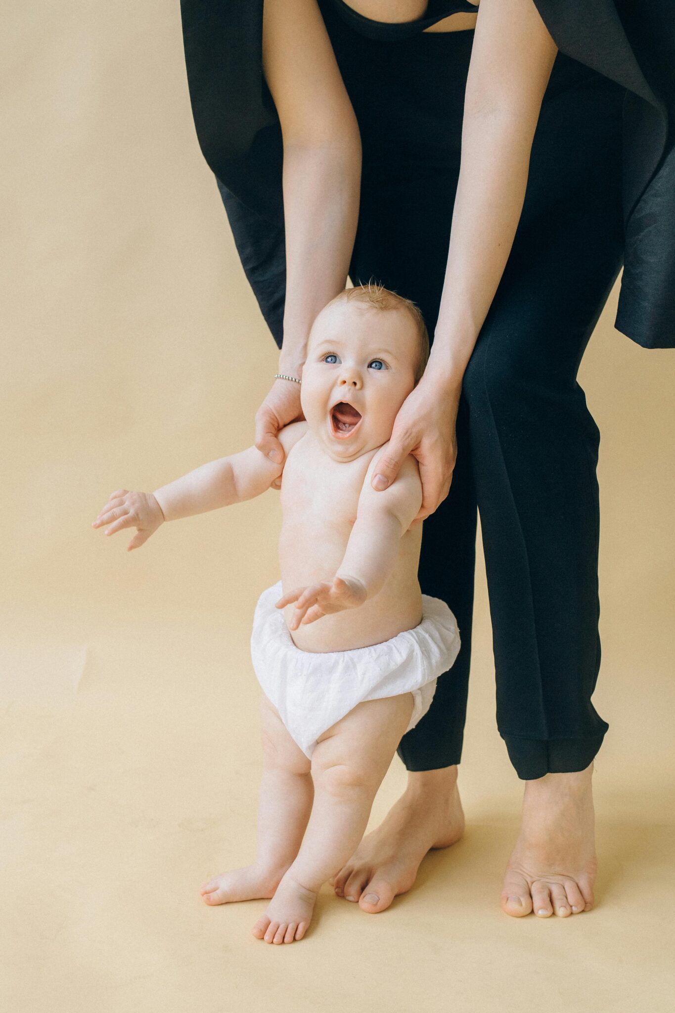 Joyful baby in a diaper with parent's support against a beige background.